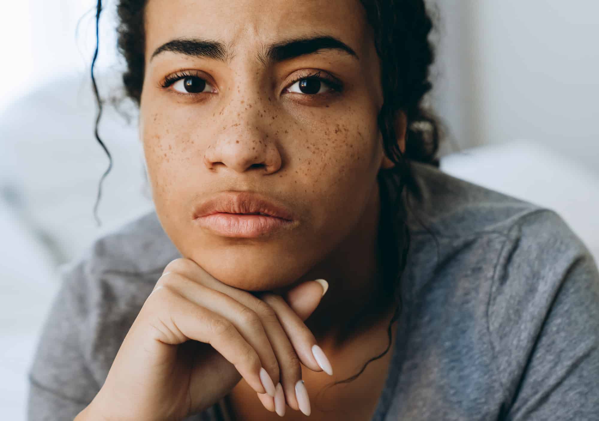 Serious woman with freckles, curly hair, and gray shirt.